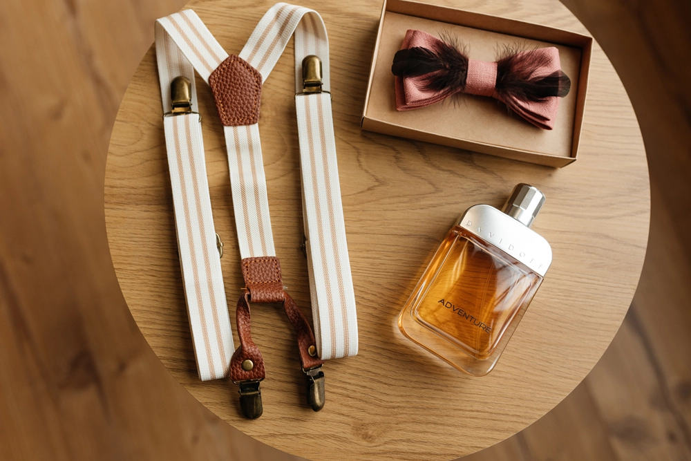 Stilvolle Herren-Accessoires für die Hochzeit: Hosenträger, Fliege und Parfüm als Flatlay arrangiert.