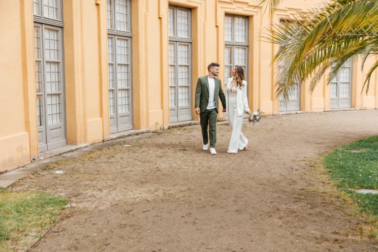 Brautpaar läuft händchenhaltend und lachend vor der Orangerie Erlangen bei ihrer standesamtlichen Hochzeit.
