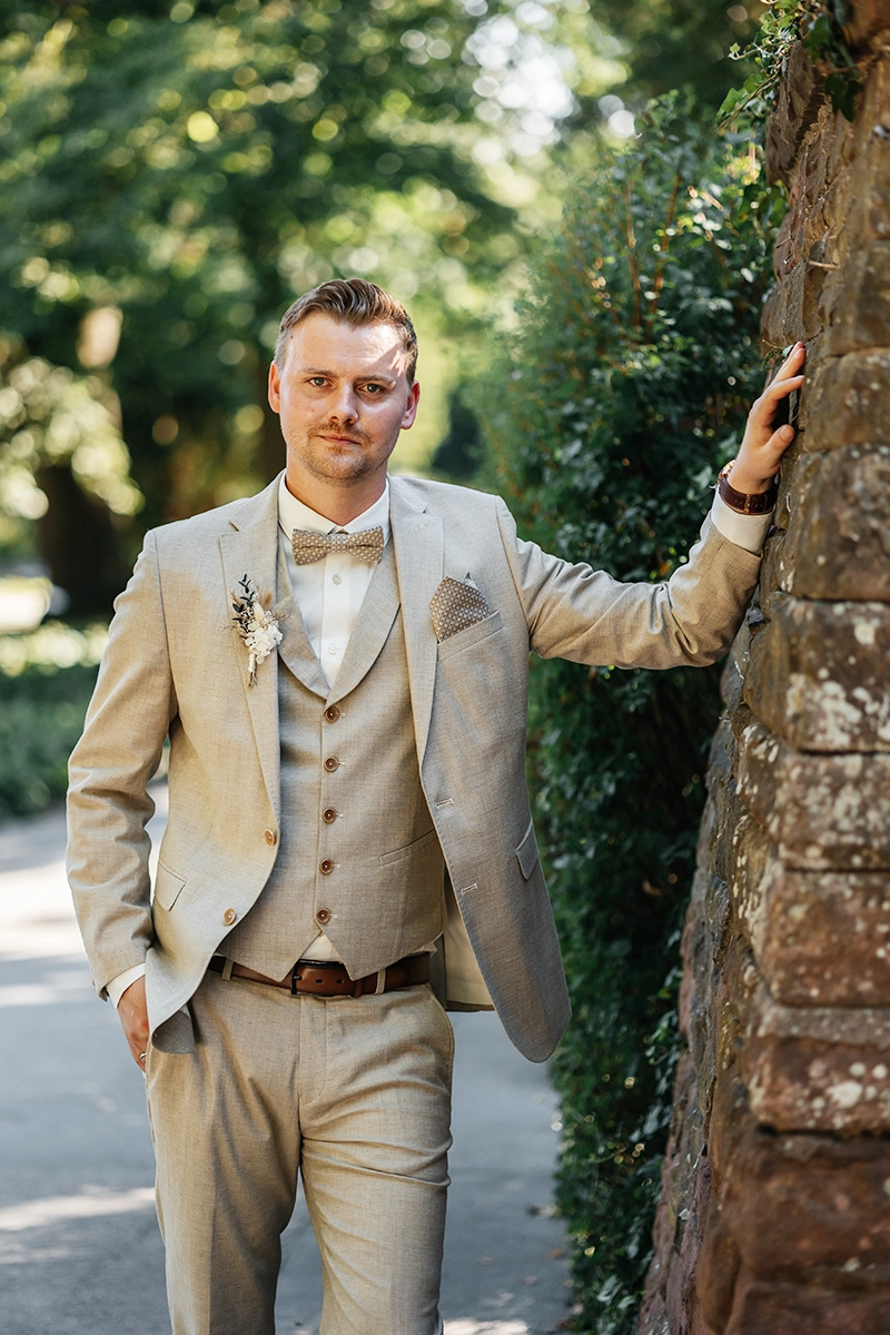 Bräutigam im beigen Leinen-Anzug lehnt lässig an einem Baum im Stadtpark Fürth.