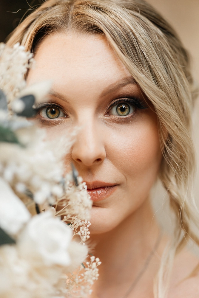 Künstlerische Nahaufnahme der Braut, halb verdeckt durch unscharfe weiße Blumen im Vordergrund.