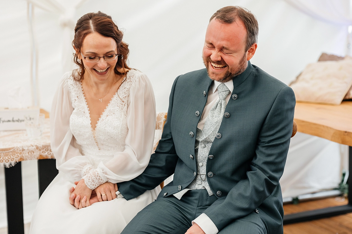 Braut und Bräutigam sitzen im Trauzelt und lachen miteinander