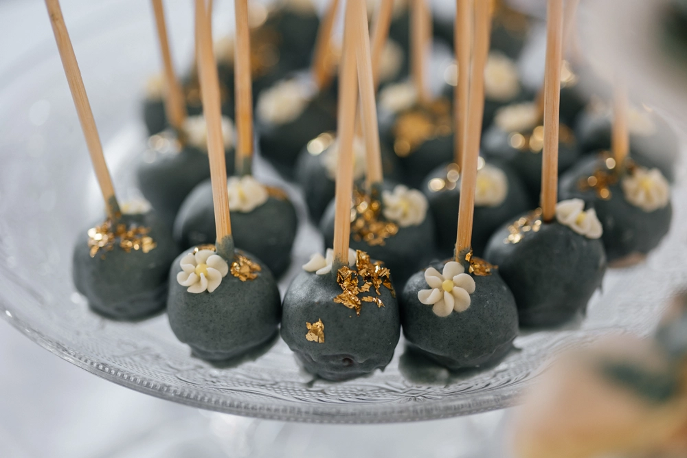 Dunkle Cake-Pops mit Goldverzierung auf dem Sweet Table der Hochzeit.