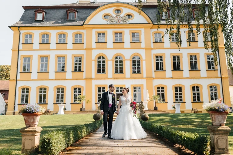 Brautpaar läuft händchenhaltend vor der gelben Barockfassade von Schloss Jägersburg