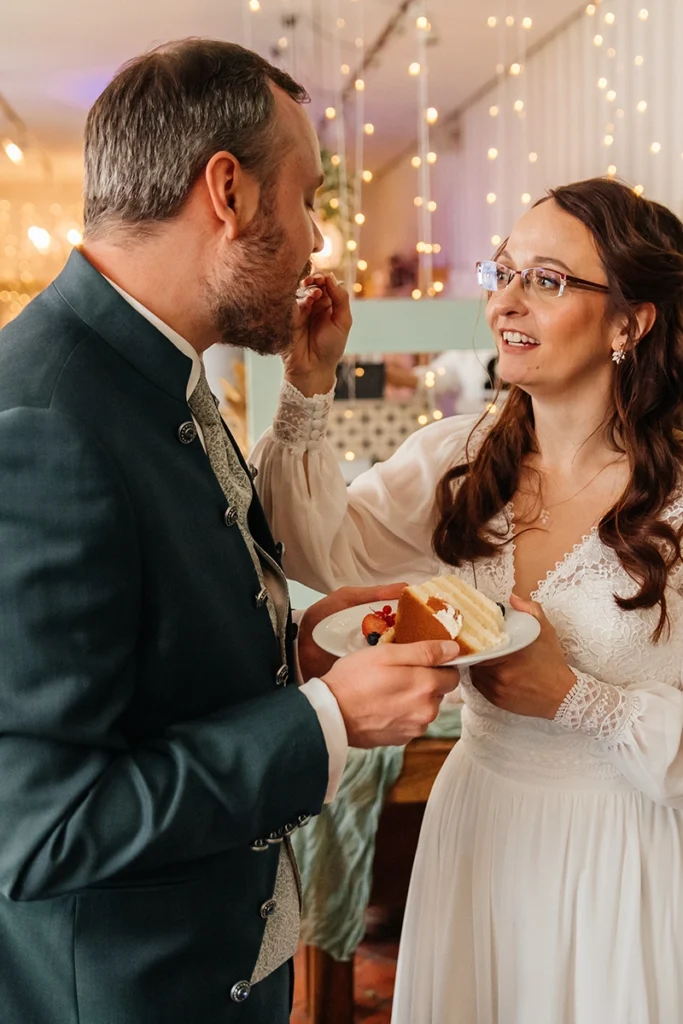 Braut füttert den Bräutigam beim Tortenanschnitt mit einem Stück Hochzeitstorte