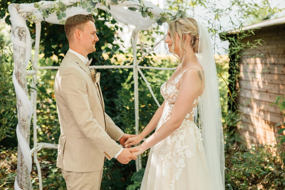 Braut und Bräutigam halten sich während der Zeremonie unter dem weißen Traubogen an den Händen.