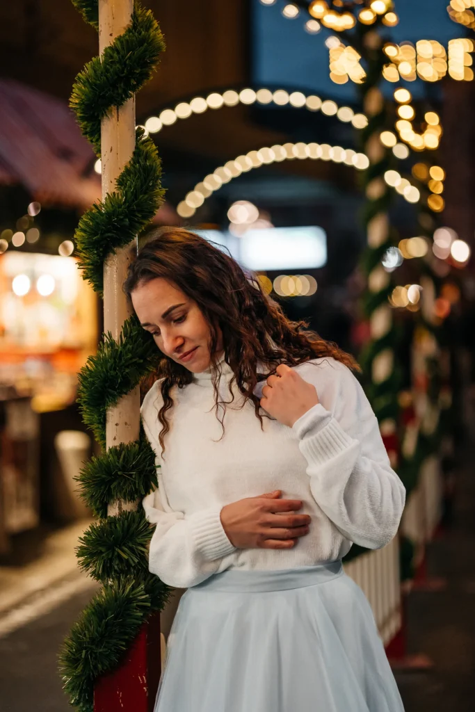 Winterliches Portrait einer Frau an festlich dekoriertem Pfosten mit schönen Lichterbögen im Hintergrund.