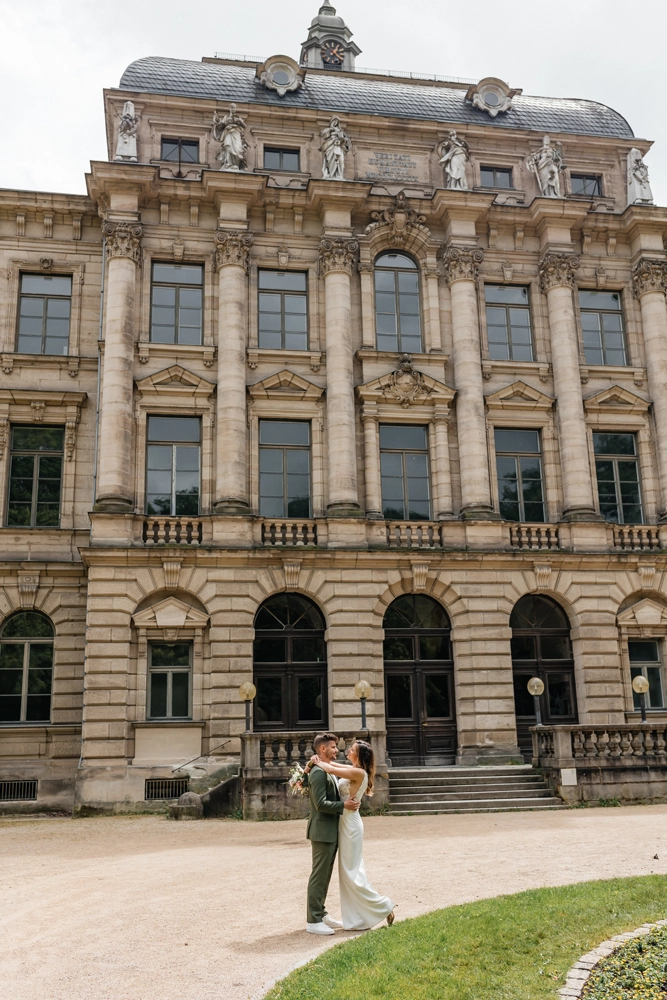 Weitwinkelaufnahme der imposanten Barock-Fassade in Erlangen mit dem Brautpaar klein im Vordergrund für dramatischen Effekt.