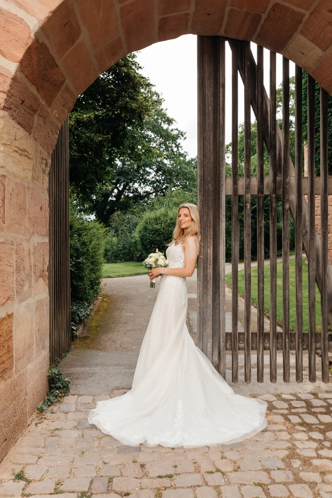     Braut steht allein im historischen steingemauerten Torbogen, Editorial Brautportrait mit Schleppe.