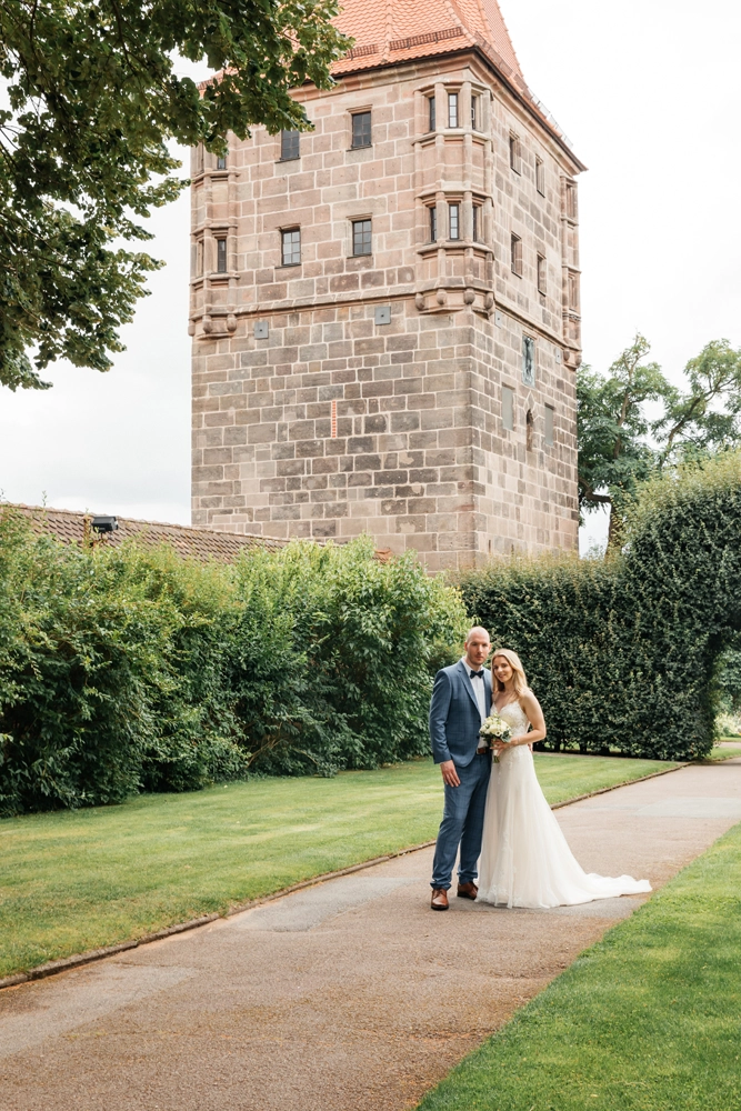 Brautpaar spaziert entspannt auf einem Weg vor dem Turm der Nürnberger Kaiserburg.