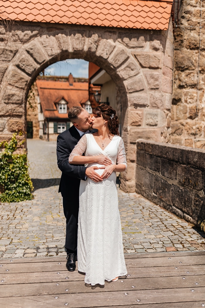 Brautpaar küsst sich im steingemauerten Torbogen, intimer Moment