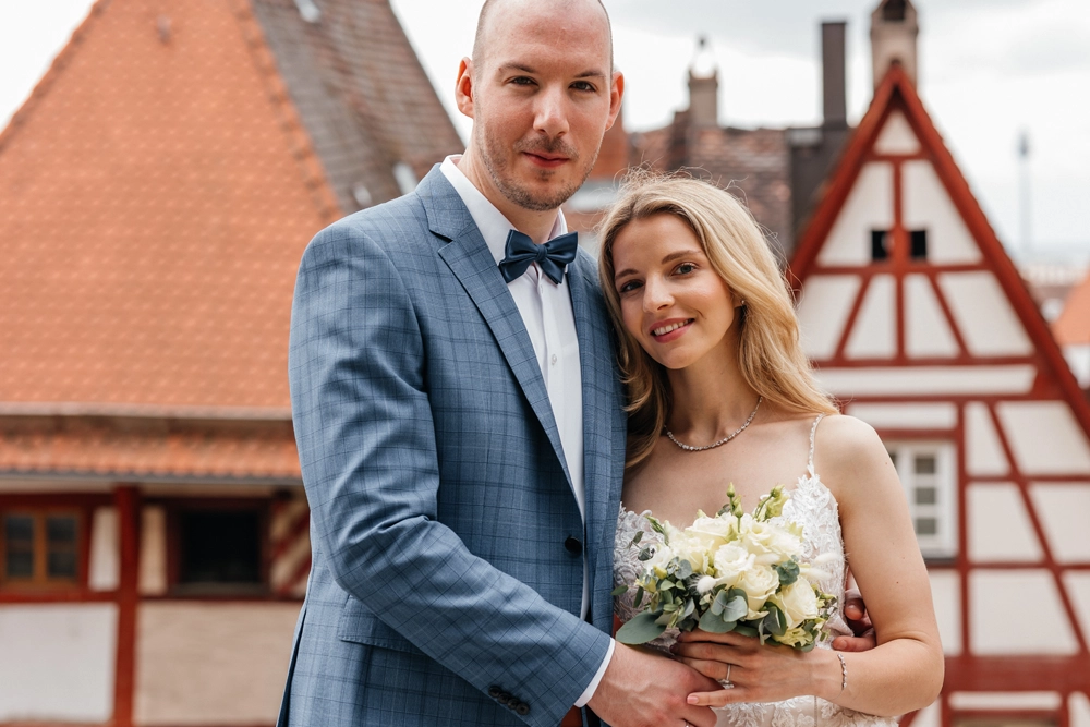 Brautpaar steht auf einer Terrasse mit Blick auf Nürnberger Fachwerkhäuser, elegantes City-Hochzeitsfoto.