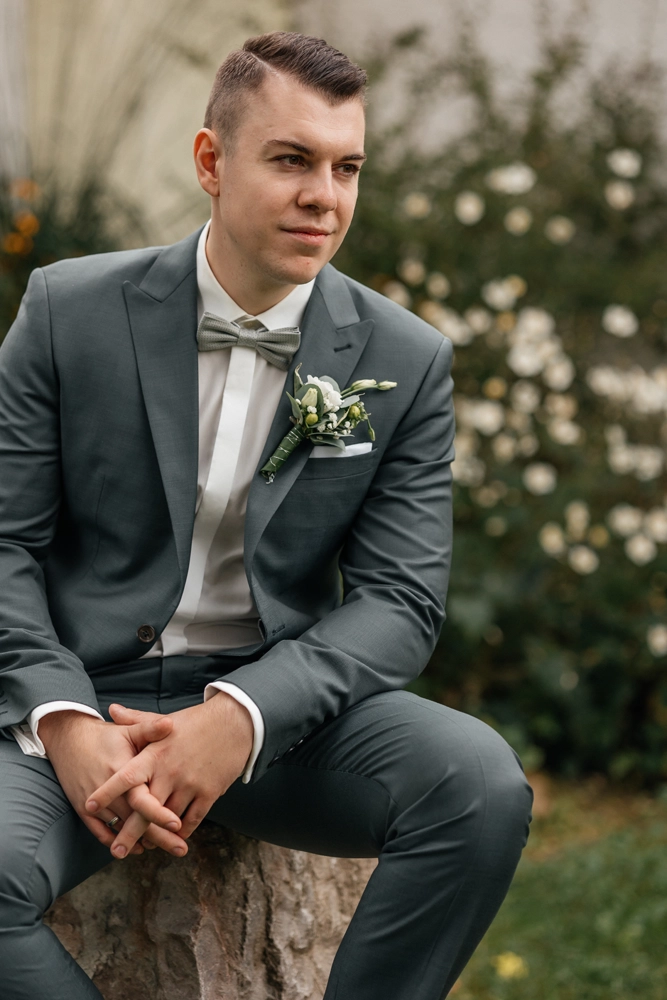 Lässiges Portrait des Bräutigams im grüner Anzug mit Fliege, sitzend auf einem Stein.