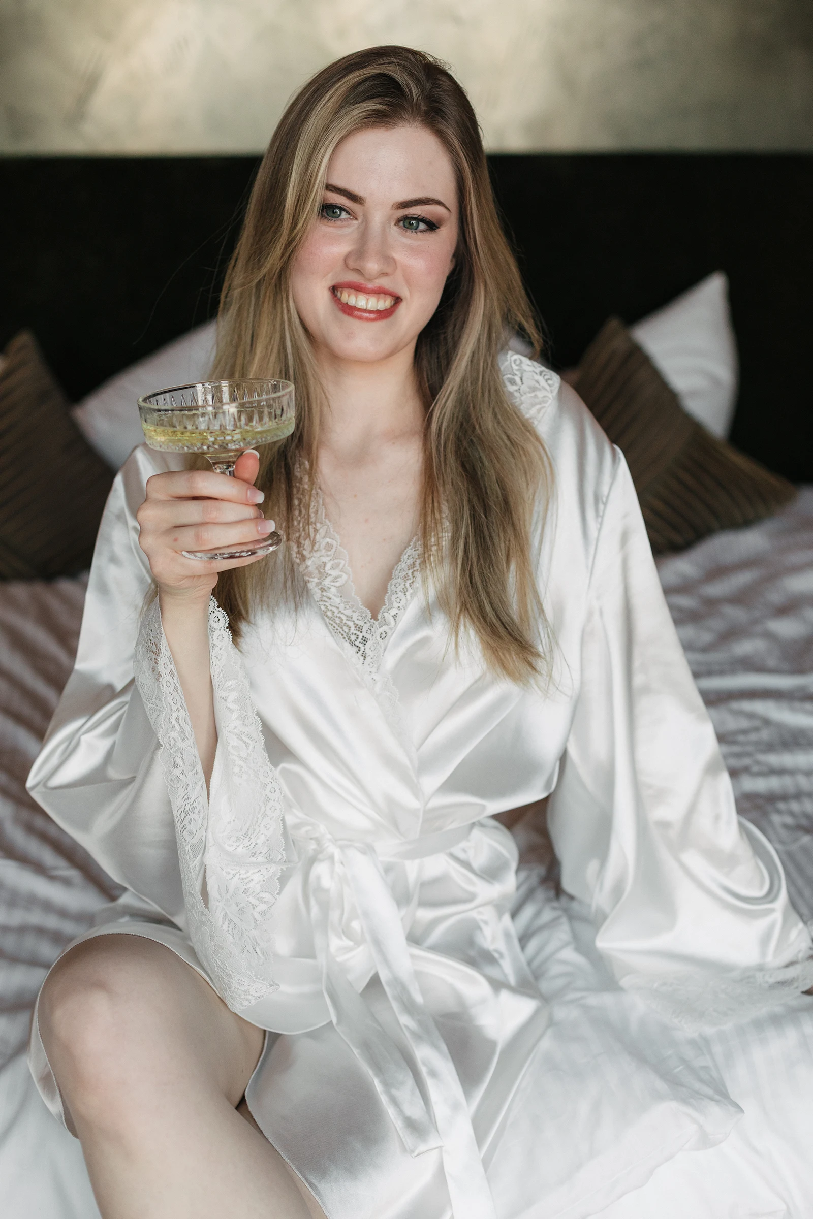 Lächelnde Braut im Bademantel hält ein Sektglas, Vorfreude auf die Hochzeit.