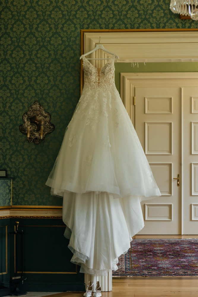 Weißes Brautkleid hängt vor einer grünen historischen Tür im Schloss