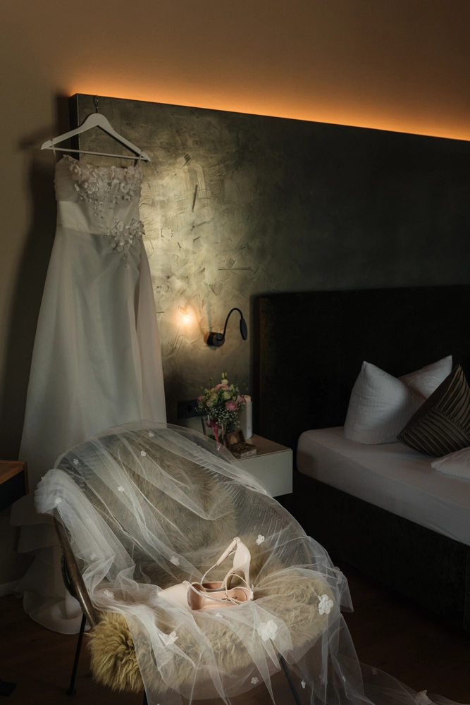 Das Brautkleid hängt stimmungsvoll beleuchtet im Hotelzimmer bereit für das Anziehen.