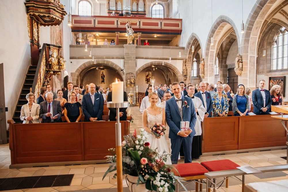 Brautpaar kniet während der Zeremonie vor dem Altar, Gäste im Hintergrund.