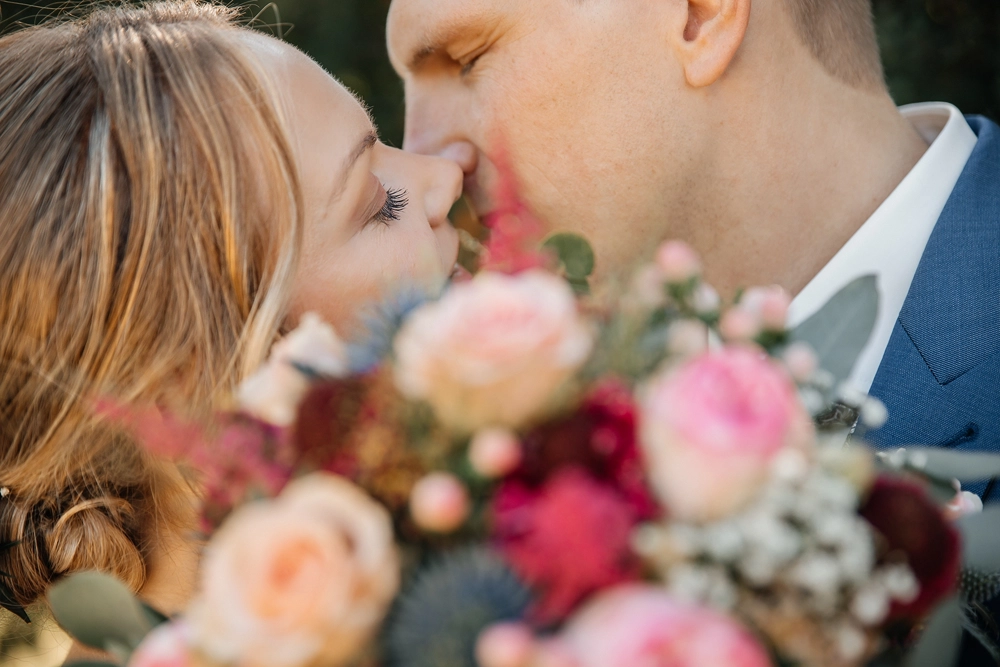 Romantischer Kuss des Brautpaares, halb verdeckt durch den bunten BrautstrauĂź.