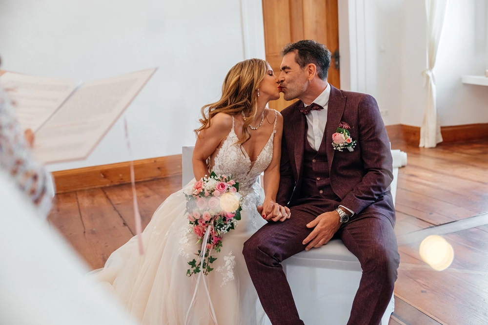 Emotionaler Moment: Braut und Bräutigam küssen sich sitzend, sie hält ihren Brautstrauß.