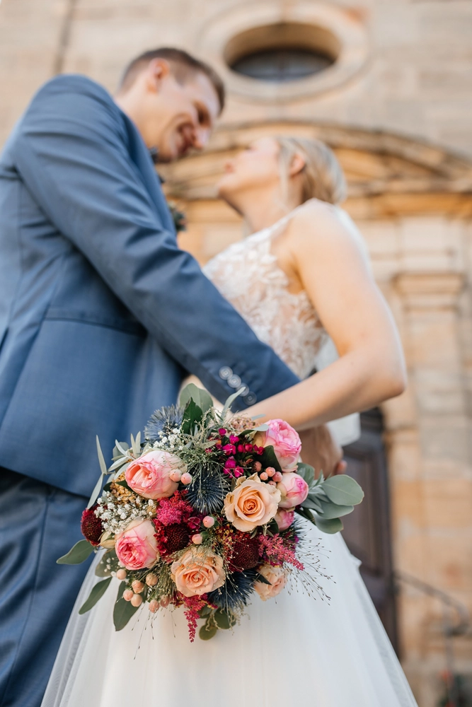 Brautpaar steht eng umschlungen unter einem historischen Sandsteinbogen der Kirche.
