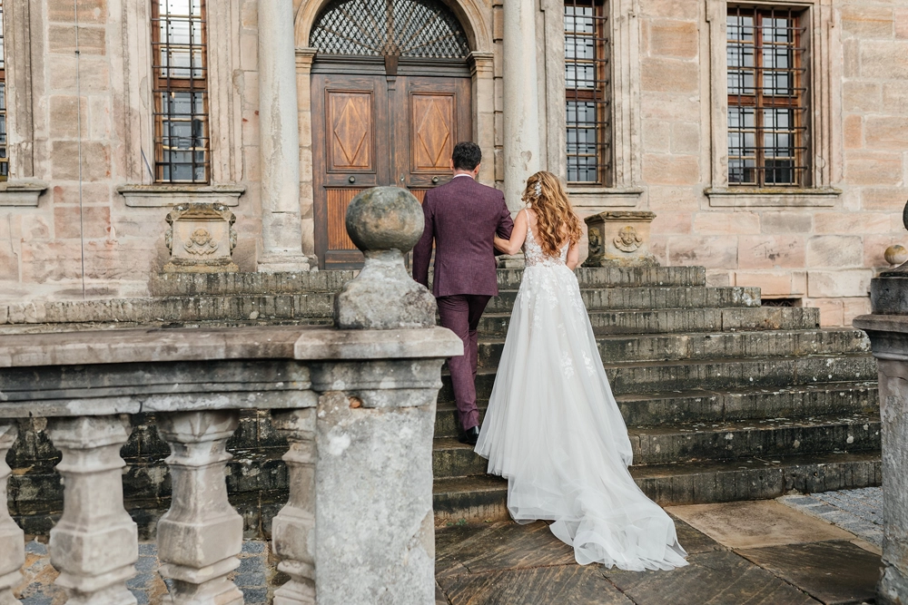 Braut und Bräutigam stehen Hand in Hand vor der historischen Holztür des Schlosses.