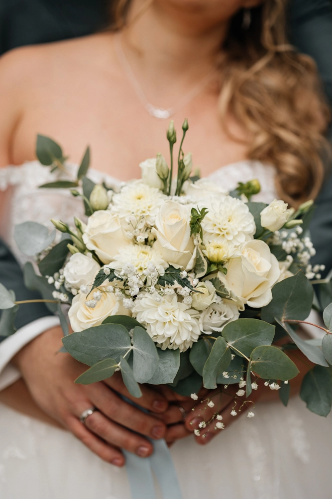 Brautstrauß aus weißen Rosen und Eukalyptus, Nahaufnahme vor dem Brautkleid.
