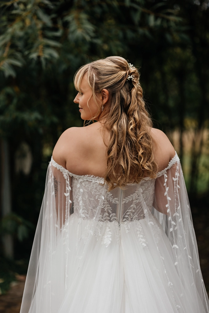 Portrait der Braut von hinten, Fokus auf offene Lockenfrisur und die Details der bestickten Ärmel.