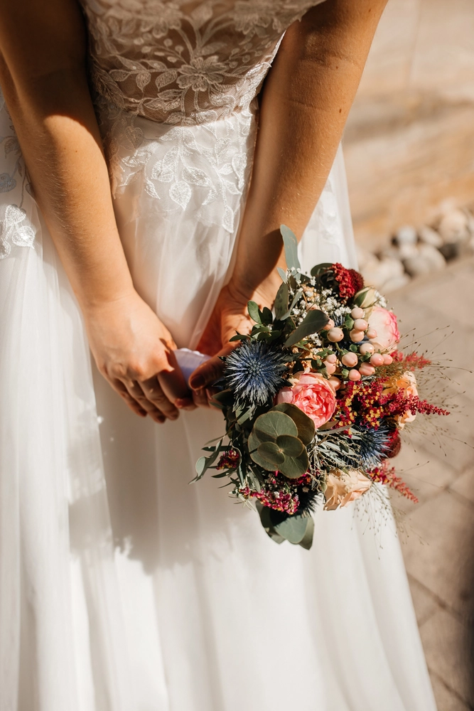Close-Up der Brauthände auf dem weißen Spitzenkleid mit Brautstrauß.