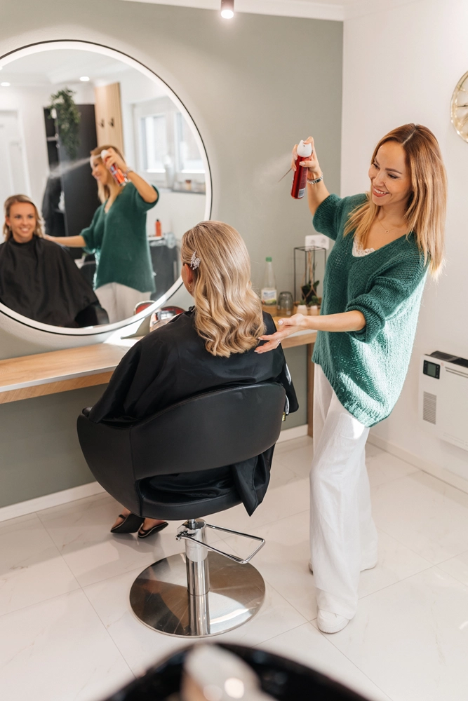 Das Finish: Fixieren der Frisur mit Haarspray – dynamisches Business-Foto im Salon.