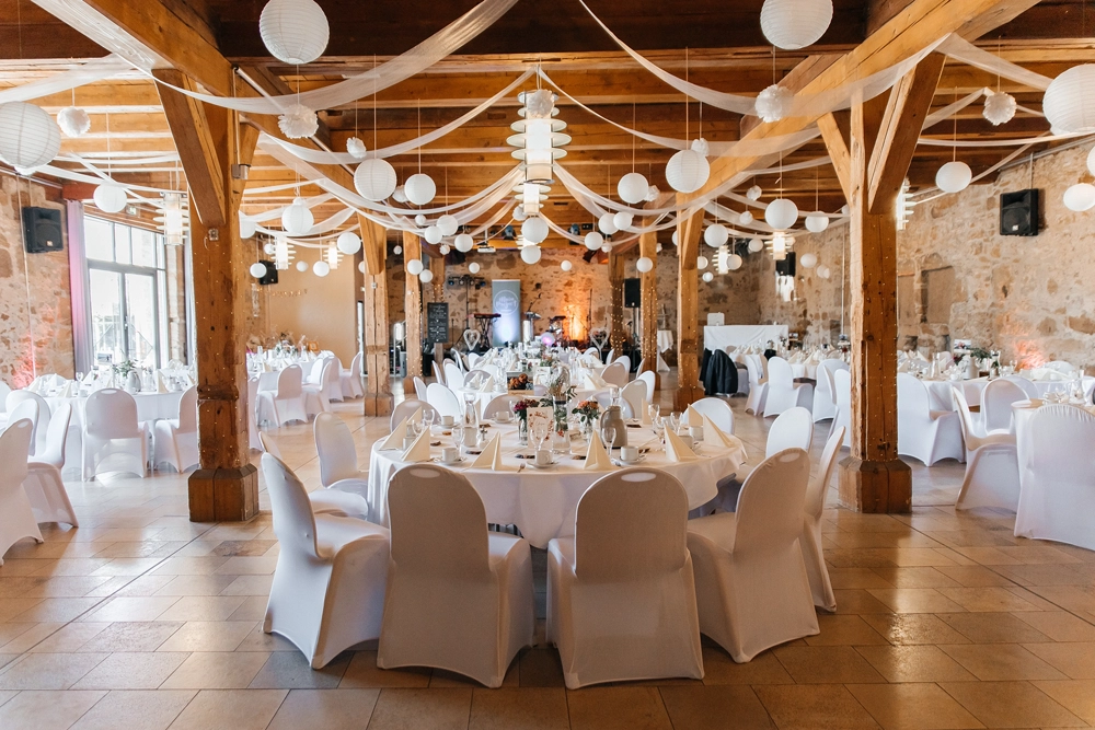 Blick in den leeren Festsaal: Runde Tische und rustikale Holzbalken-Atmosphäre.