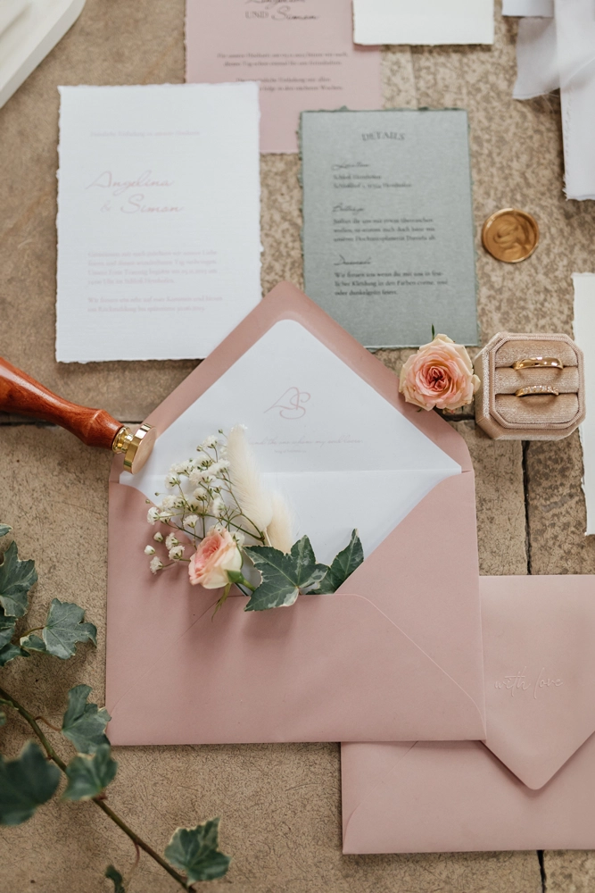 Stilvolles Flatlay der Hochzeitseinladungen in Zartrosa mit Siegel, Briefumschlägen und floralen Details.