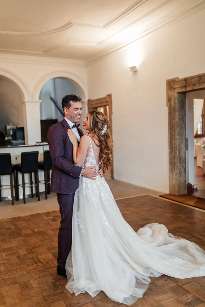 Brautpaar beim Hochzeitstanz im lichtdurchfluteten Saal. Elegante Pose vor den Bogenfenstern.