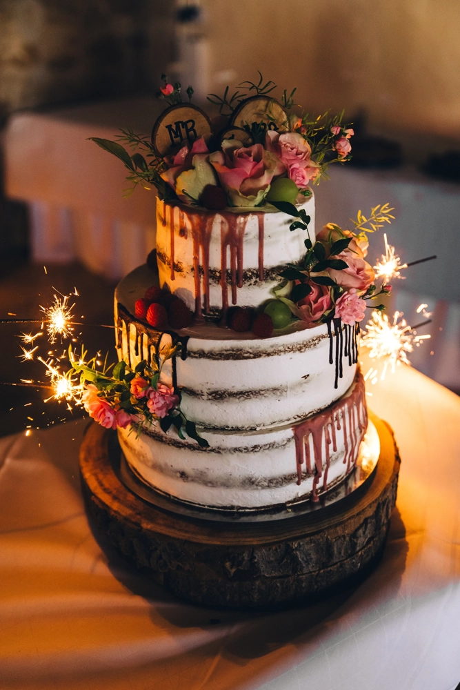 Naked Cake Hochzeitstorte mit Beeren im Dunkeln, beleuchtet von Wunderkerzen.