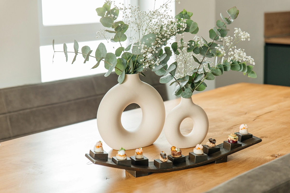 Minimalistisches Table Setting mit weißer Design-Vase und Fingerfood auf einer geschwungenen Schieferplatte.