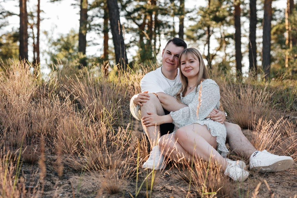 Romantisches Paarshooting zur Goldenen Stunde: Paar sitzt entspannt im hohen Gras im Nürnberger Wald.