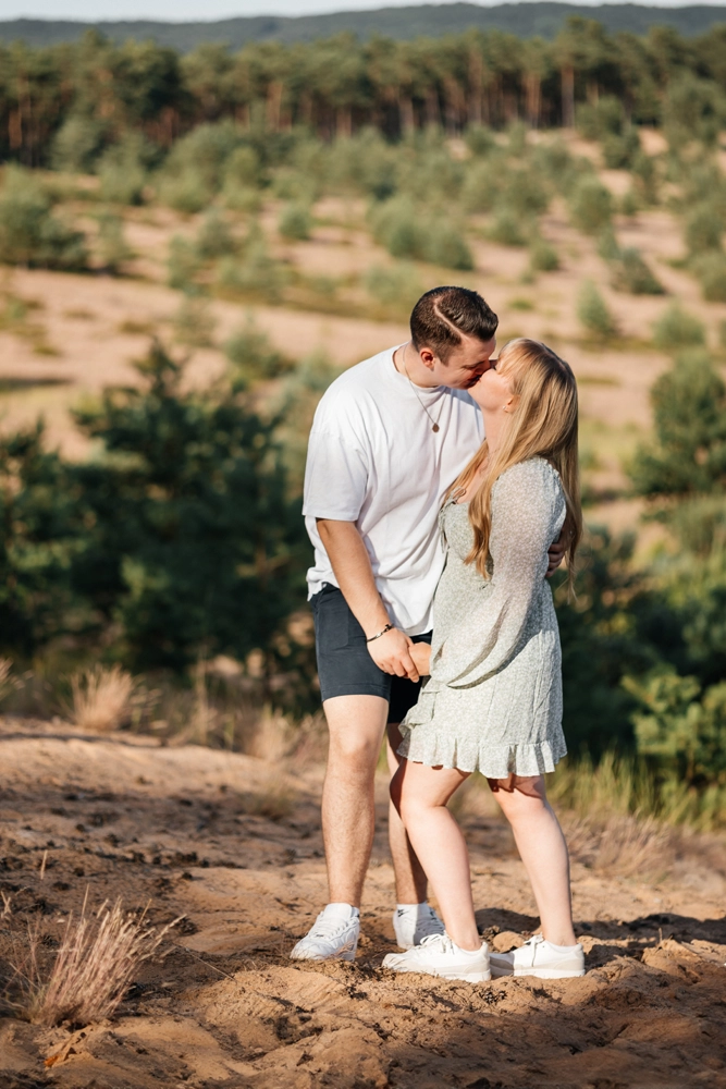 Romantischer Kuss im Stehen auf sandigem Waldboden im Gegenlicht.
