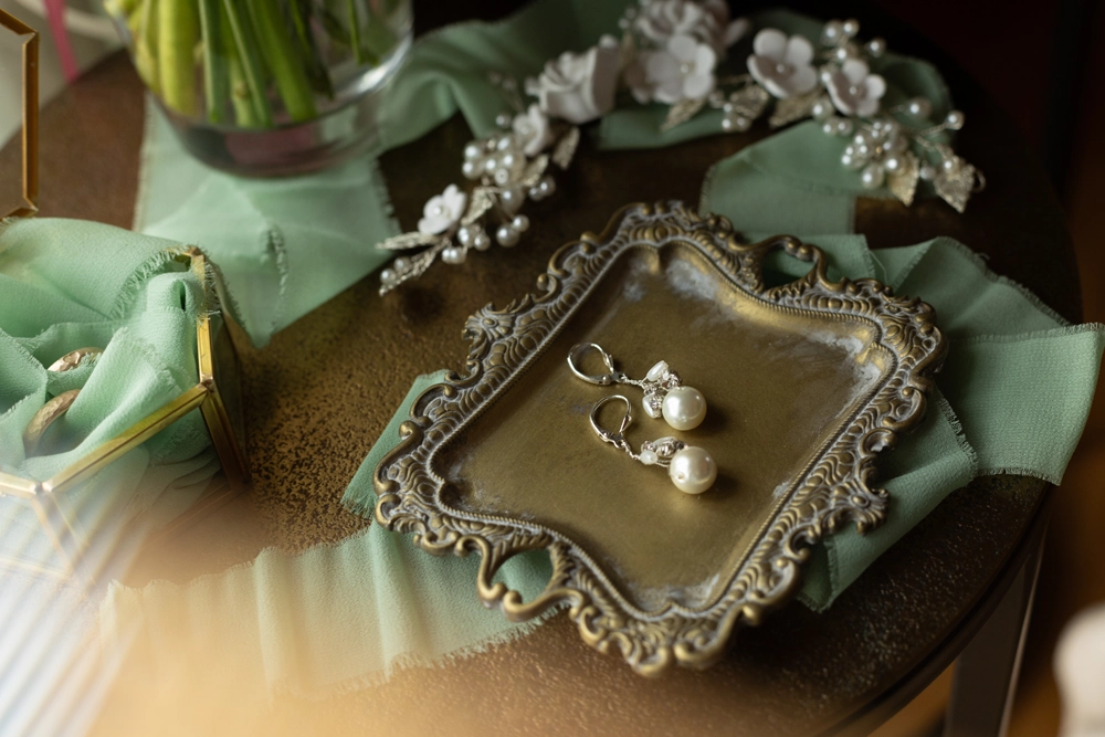 Detailaufnahme von Perlenohrringen und Haarschmuck auf einem goldenen Vintage-Tablett.