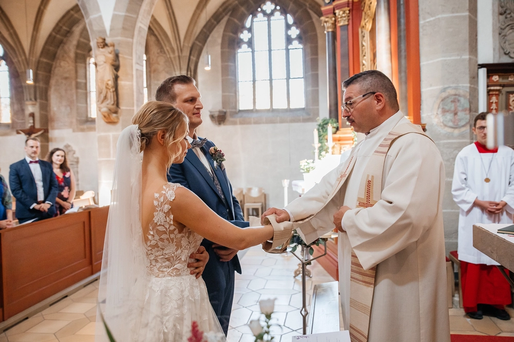 Detailaufnahme der Hände: Der Pfarrer segnet den Ringwechsel.