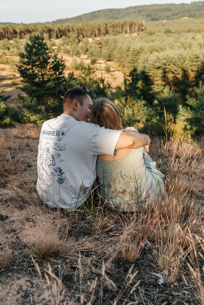 Ruhiger Moment: Paar sitzt im Gras mit dem Rücken zur Kamera und blickt in die Landschaft.
