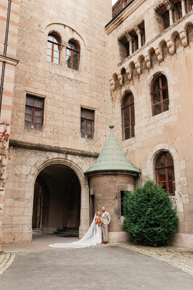 Imposante Architektur-Aufnahme im Innenhof von Schloss Faber-Castell: Brautpaar steht klein vor großen Steinmauern, Torbogen und Turm.