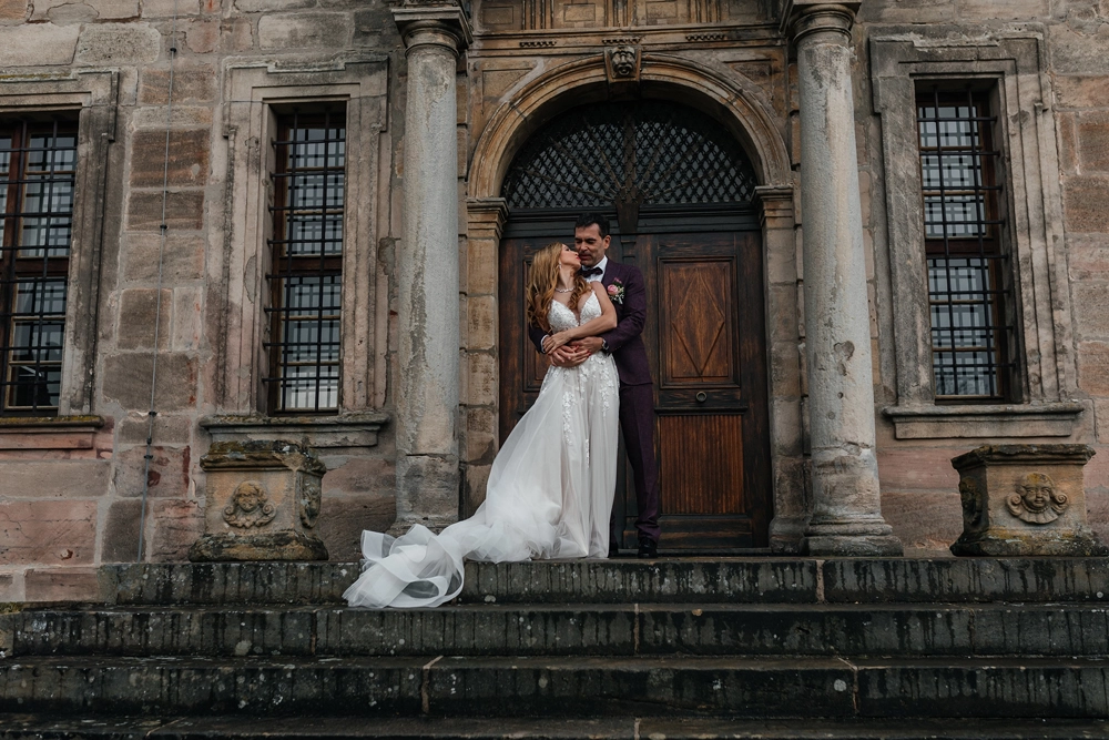Imposante Außenansicht von Schloss Hemhofen mit Brautpaar auf der Steintreppe. Editorial Look.