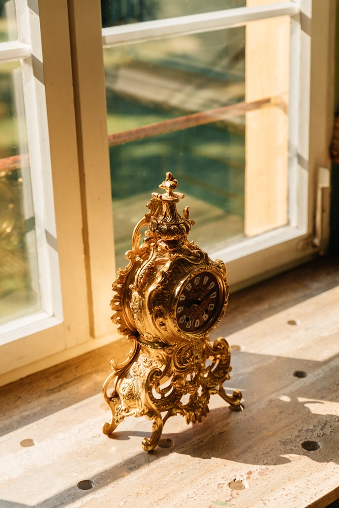 Antike goldene Uhr im warmen Sonnenlicht auf einer Fensterbank. Stimmungsvolles Detail der Hochzeitslocation Schloss Jägersburg, fotografiert von Natalia Fichtner