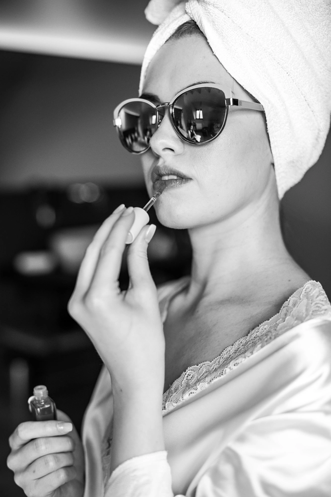 Schwarz-Weiß Aufnahme: Braut mit Sonnenbrille zieht Lippenstift nach, cooler Editorial Look.