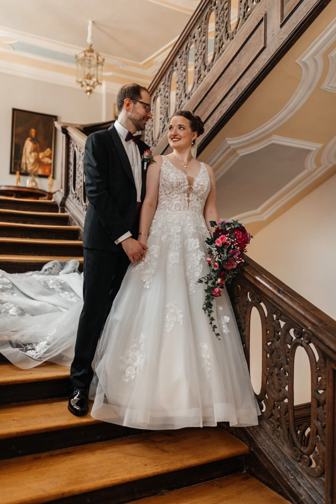 Brautpaar steht auf der historischen Holztreppe im Schloss Jägersburg