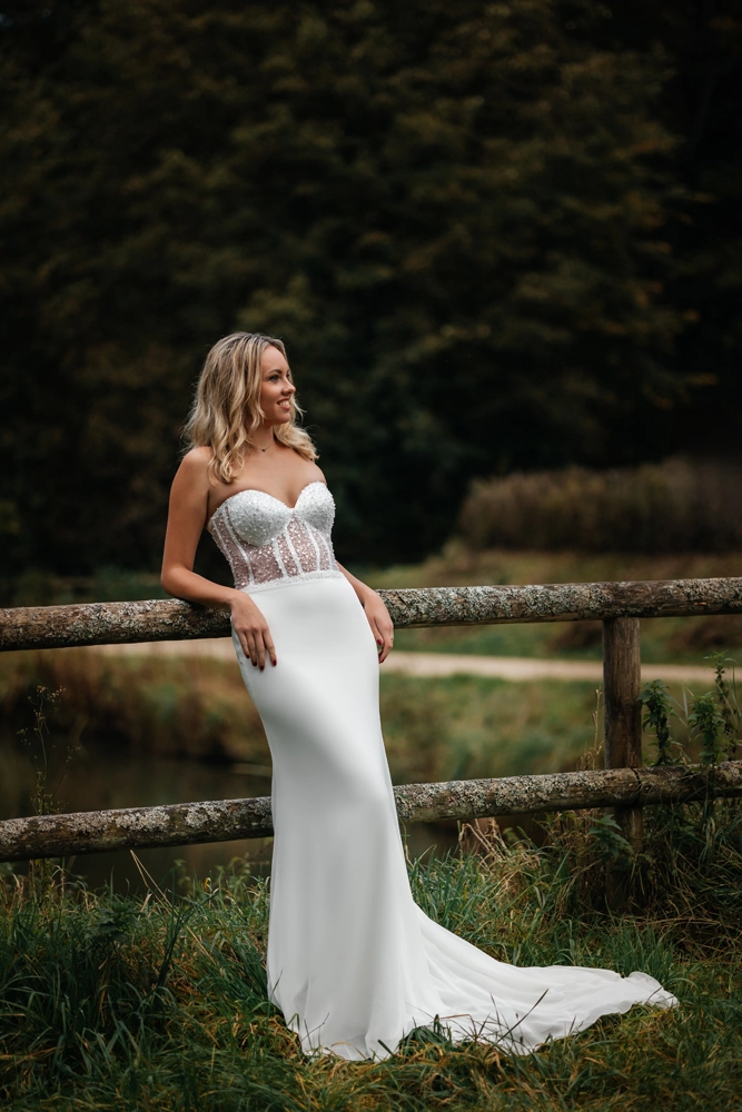 Ganzkörper-Portrait der Braut, die entspannt an einem rustikalen Holzzaun in der Natur lehnt.