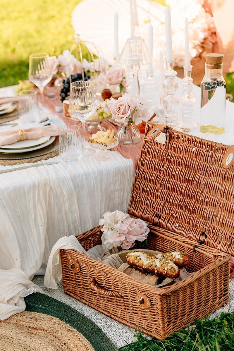 Klassischer Picknickkorb auf einer weißen Decke beim eleganten Setup für einen Antrag im Schlosspark.
