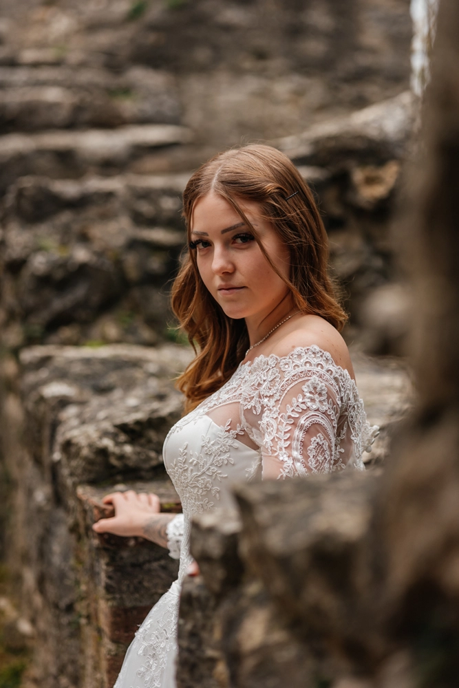 Nahaufnahme Portrait der Braut mit offenen, welligen Haaren und Spitzenkleid vor den historischen Mauern der Burgruine Wolfstein.
