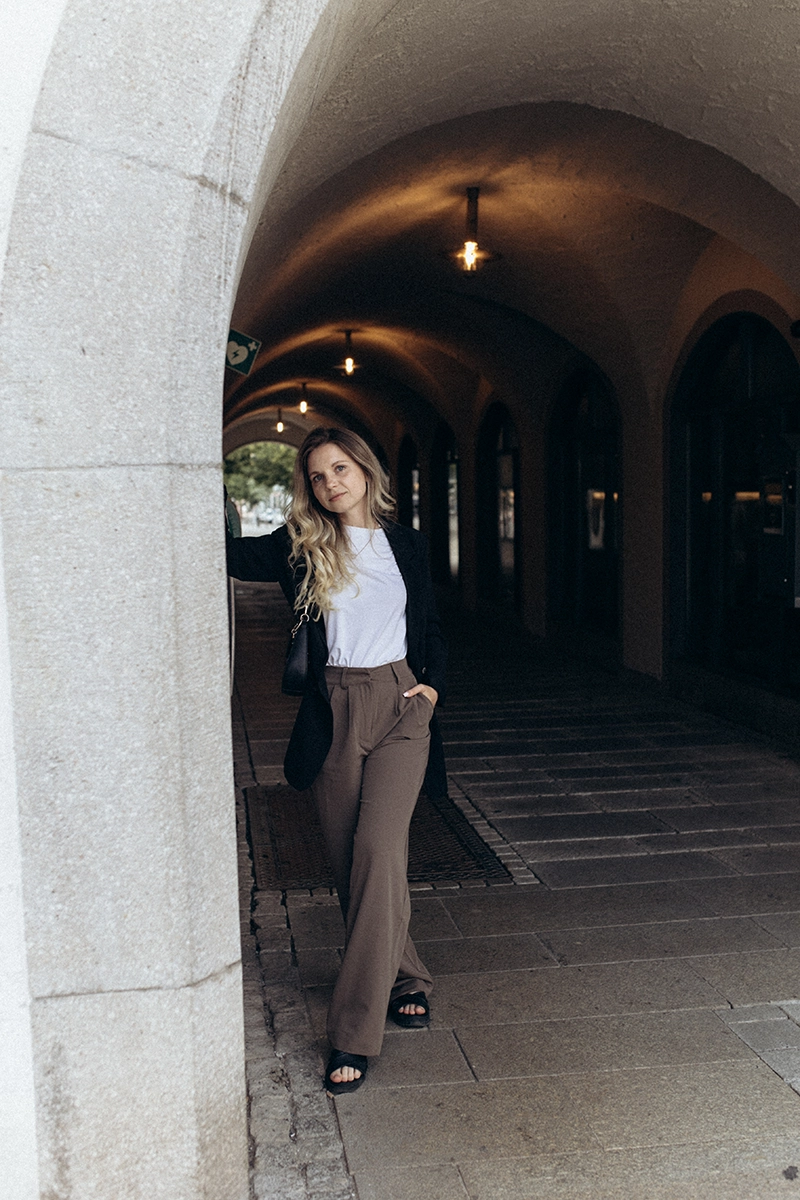 Selbstbewusste Unternehmerin lehnt entspannt an einem Steinbogen in historischen Arkaden, modernes Editorial Business Portrait in Nürnberg.