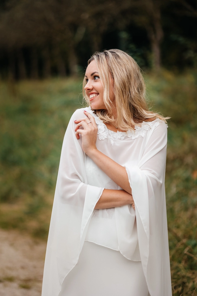 Porträtaufnahme einer lachenden Braut mit modernem Braut-Cape bei einem After-Wedding-Shooting.