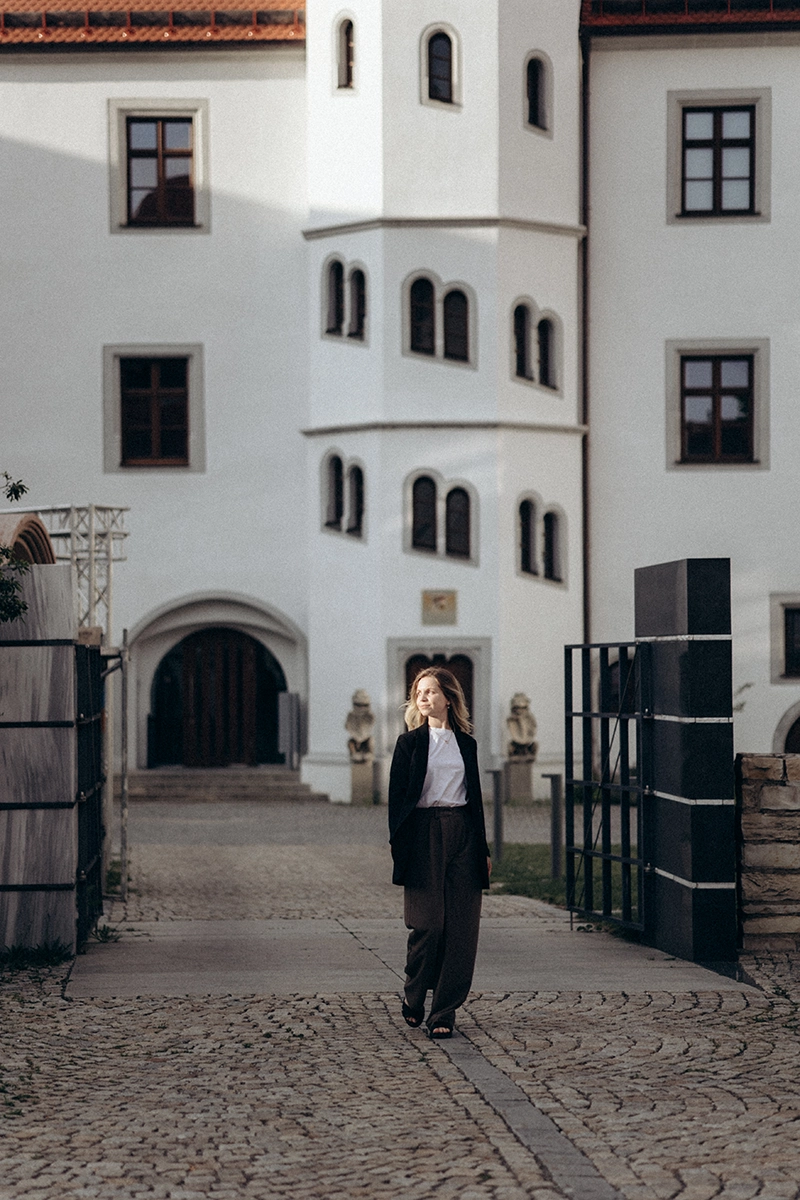 Unternehmerin im modernen Signature-Look vor der eleganten Kulisse eines weißen Schlosses, High-End Businessfotografie in Bayern.