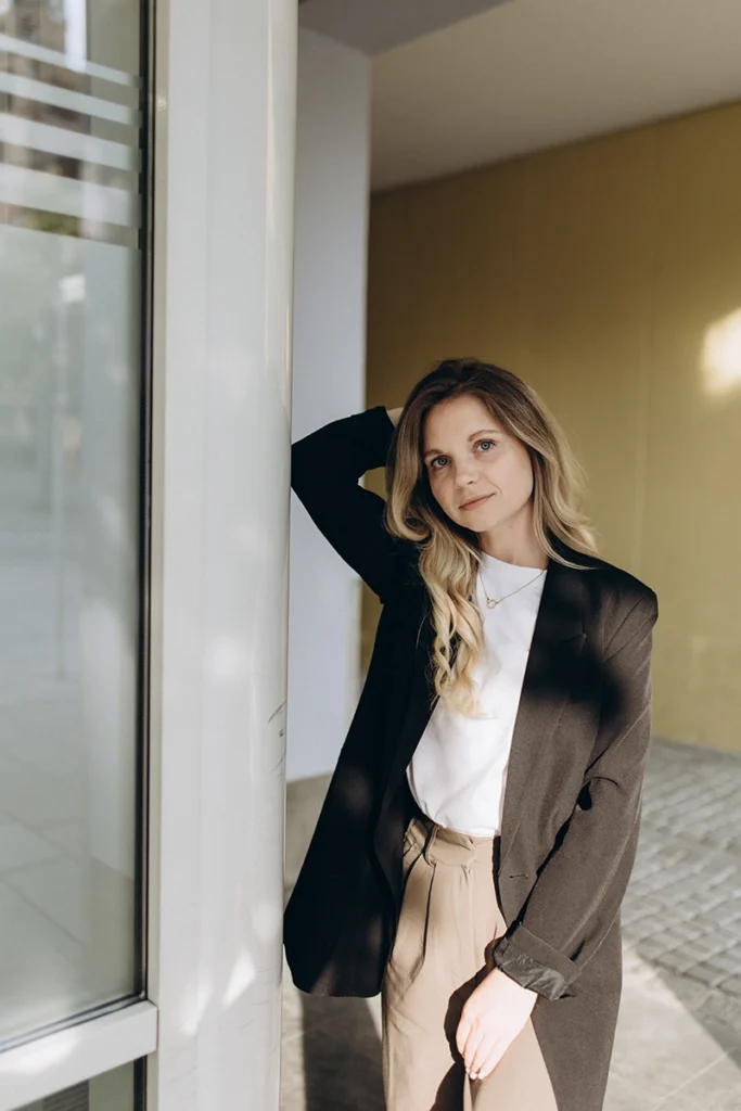 Selbstbewusste Frau im modernen Business-Look lehnt entspannt an einer sonnigen Glasfassade, Personal Branding Shooting in Neumarkt.